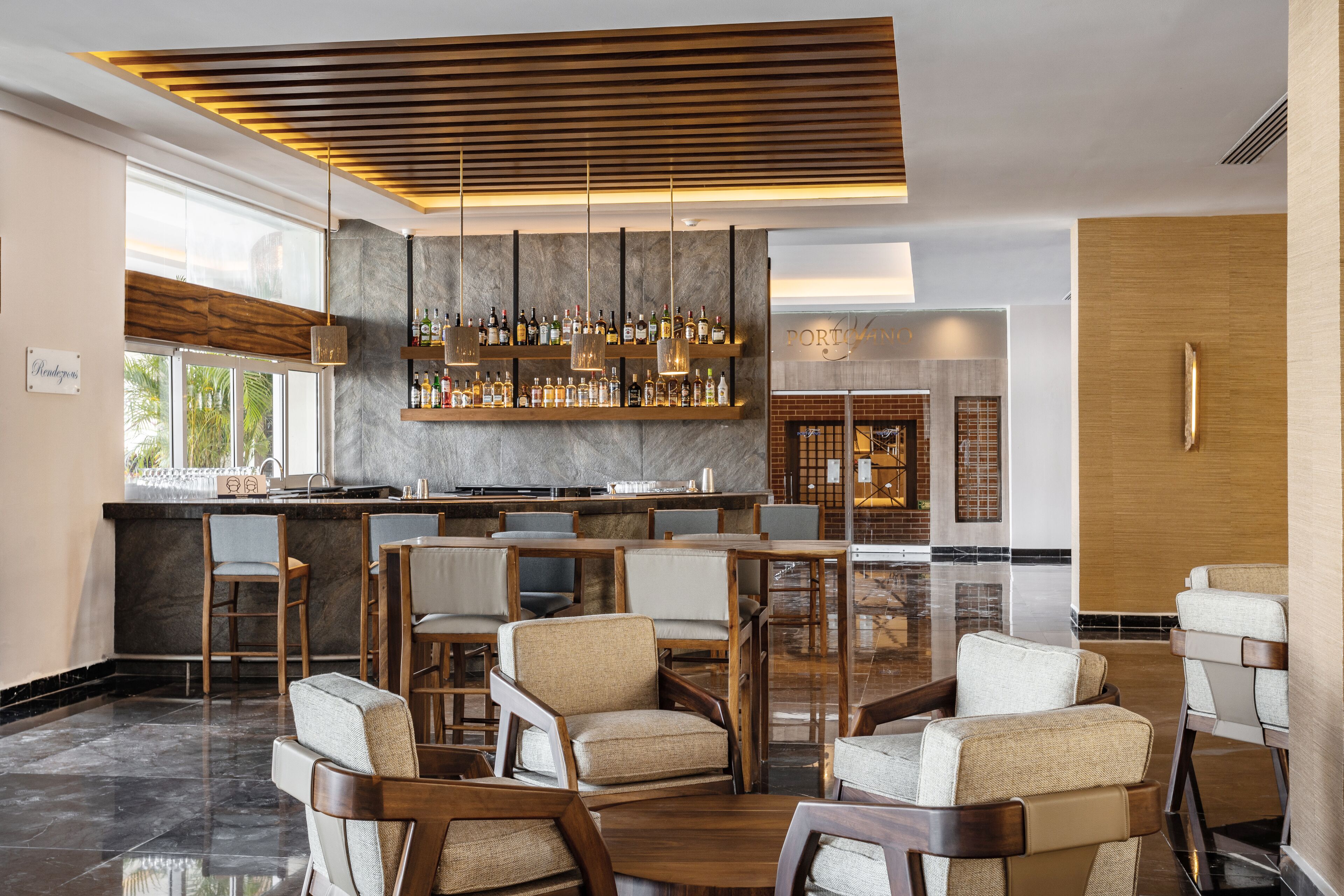 A modern bar area with a wooden ceiling, bar stools, and a variety of bottles.