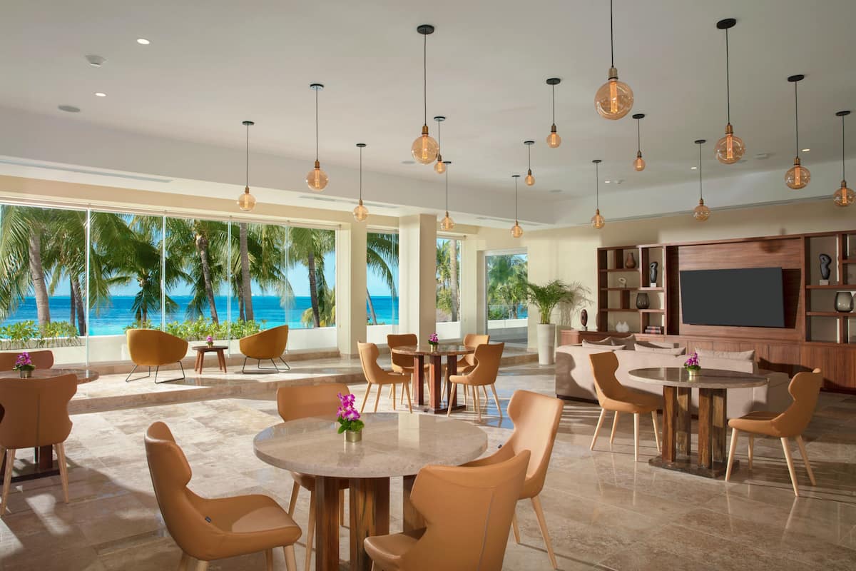 A spacious living area with multiple seating arrangements, a large TV, and a view of the ocean.