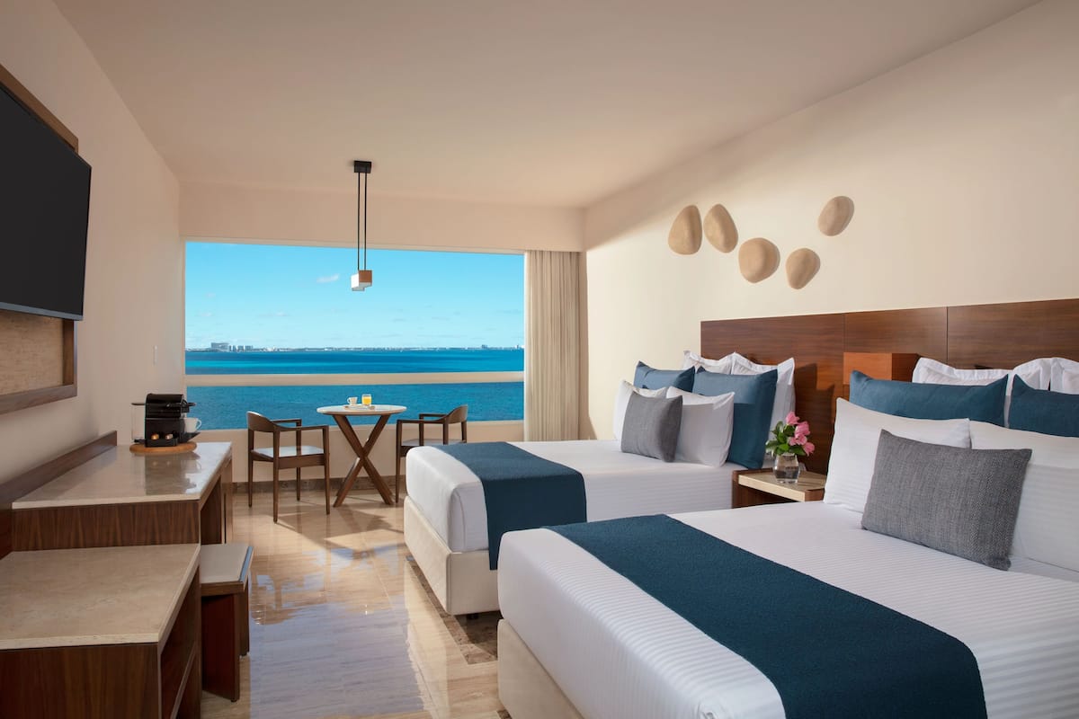 A hotel room with two beds, a desk, a chair, and a large window overlooking the sea.