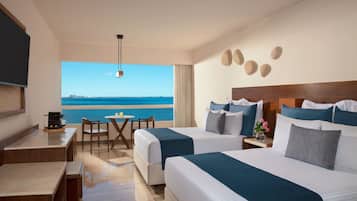 A hotel room with two beds, a desk, a chair, and a large window overlooking the sea.