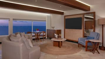 Una sala moderna con sofá, sillones, una mesa de centro y un comedor. Hay un ventanal con vistas al mar.