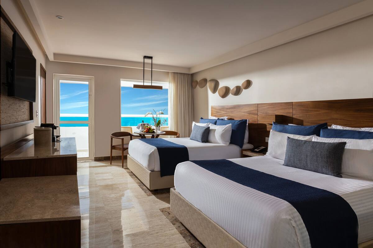 A hotel room with two beds, a desk, and a view of the ocean.