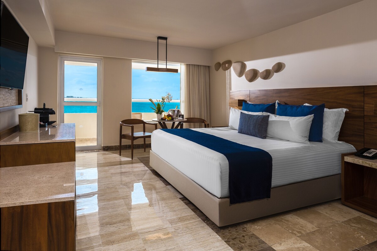 A modern hotel room with a large bed, a desk, and a view of the ocean.