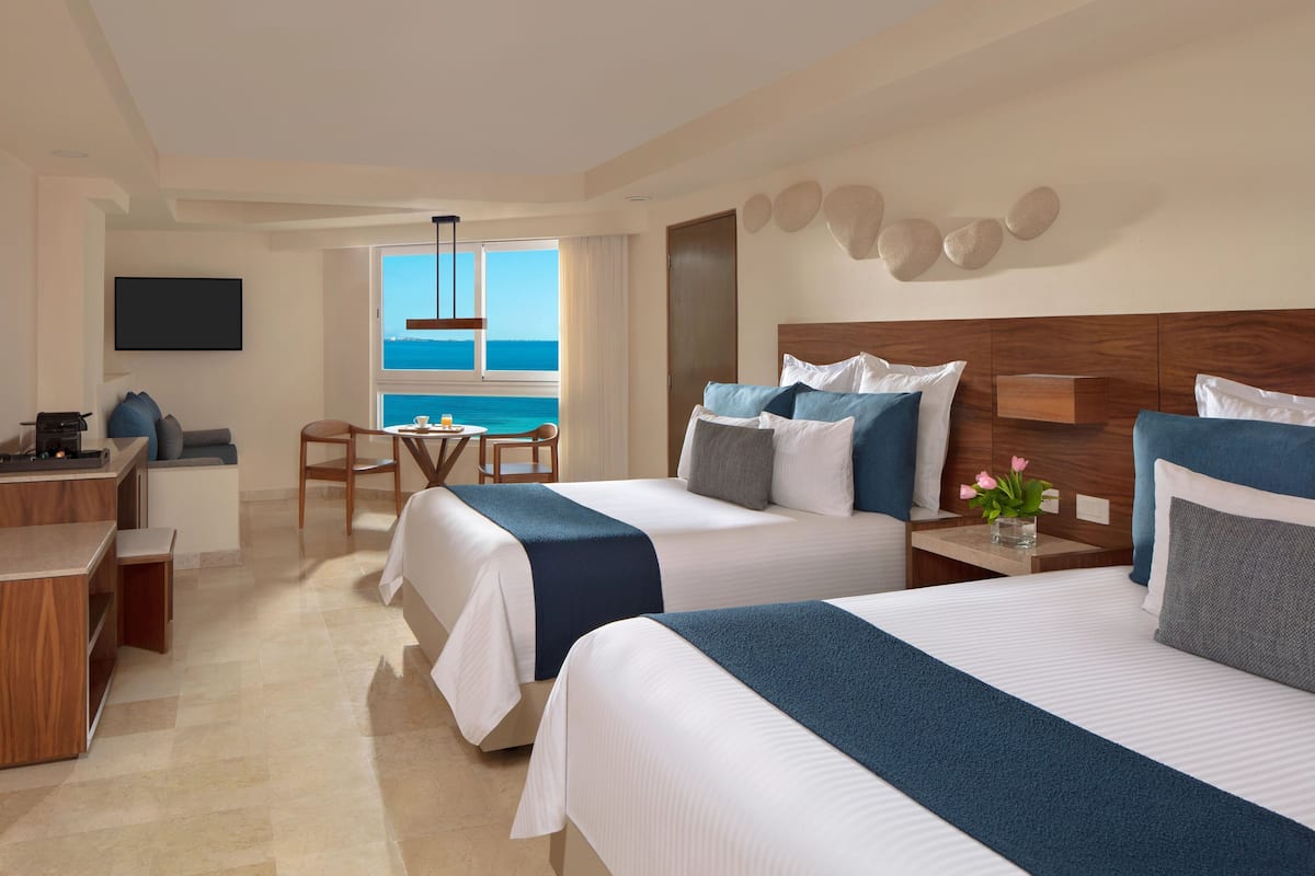 A hotel room with two beds, a desk, a chair, and a view of the sea.