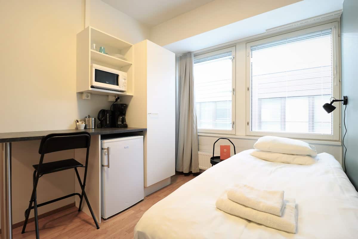 Una habitación pequeña con cama, kitchenette, escritorio y una silla.