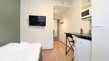 A compact hotel room with a bed, a TV, a kitchenette, and a small dining area.