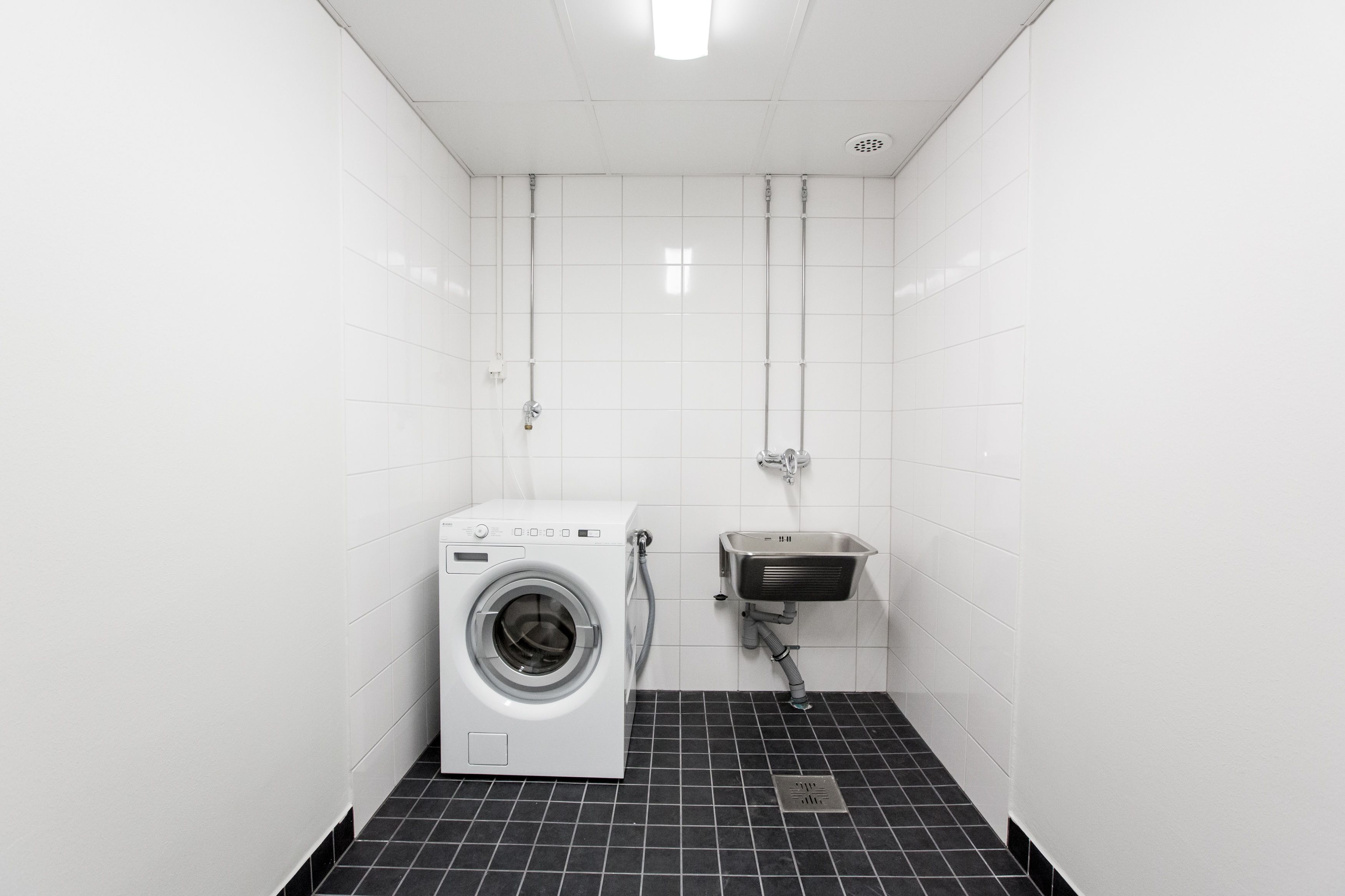 A compact, modern bathroom with a front-loading washing machine, a sink, and a shower.