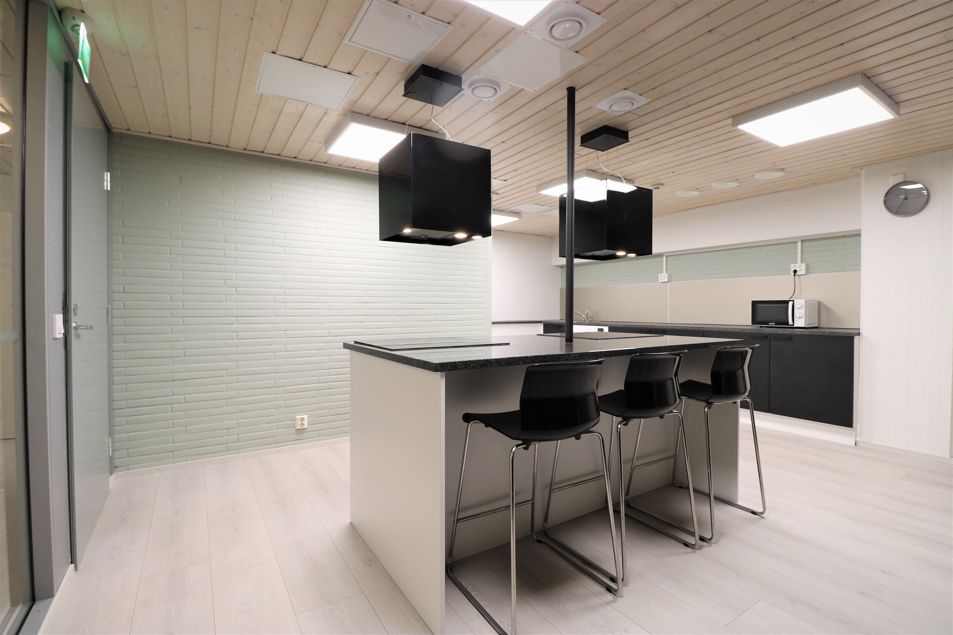 Una cocina moderna con barra, que incluye una encimera de color claro, taburetes negros y un techo de madera con iluminación empotrada.
