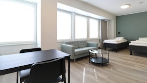 Ein modernes, helles Wohnzimmer mit einer Couch, zwei Betten, einem Esstisch und einem Couchtisch.