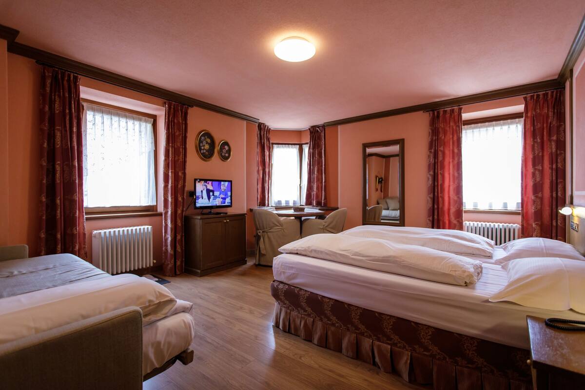 A hotel room with two beds, a desk, a television, and a window with curtains.