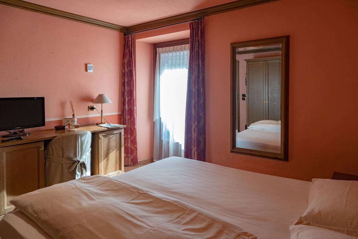 A hotel room with a bed, a desk with a television, a lamp, and a mirror.