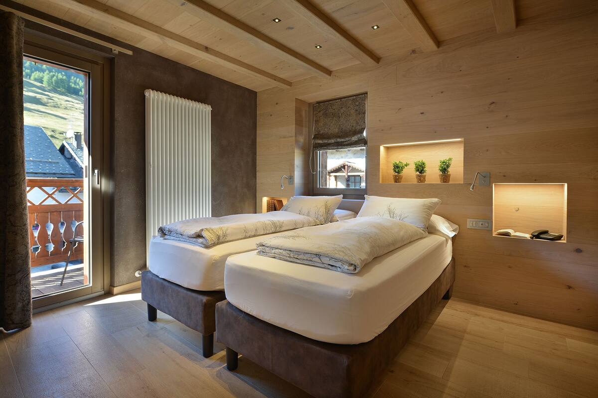 A bedroom with two beds, a window with a view, a radiator, and a shelf with plants.
