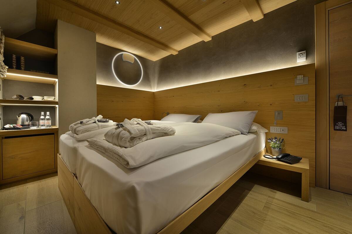 A modern hotel room with a wooden bed, bedside tables, and a built-in shelf with toiletries.