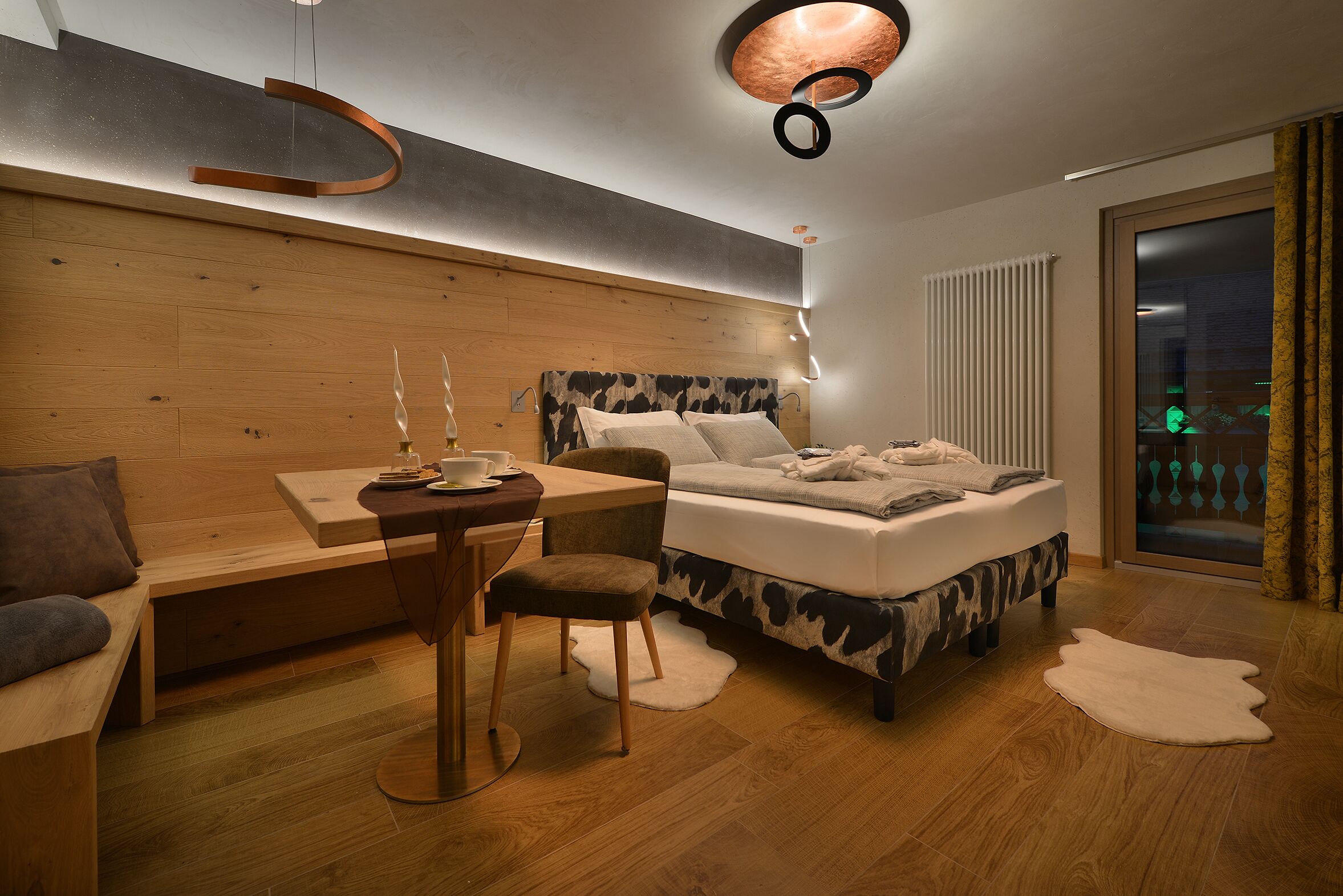 Une chambre moderne avec une tête de lit en bois, un lit à motifs imitant la peau de vache, un bureau avec une chaise et une grande fenêtre avec des rideaux.
