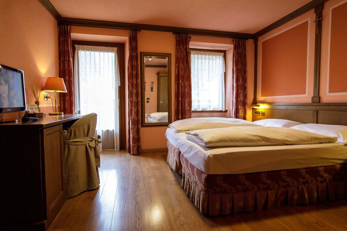 A hotel room with a bed, a desk with a lamp, and a television.
