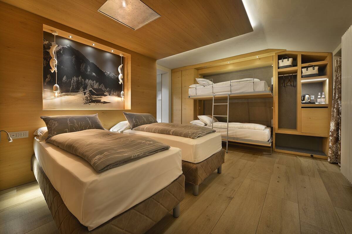 A room with two beds, a bunk bed, wooden walls, a mountain view mural, and a built-in wardrobe.