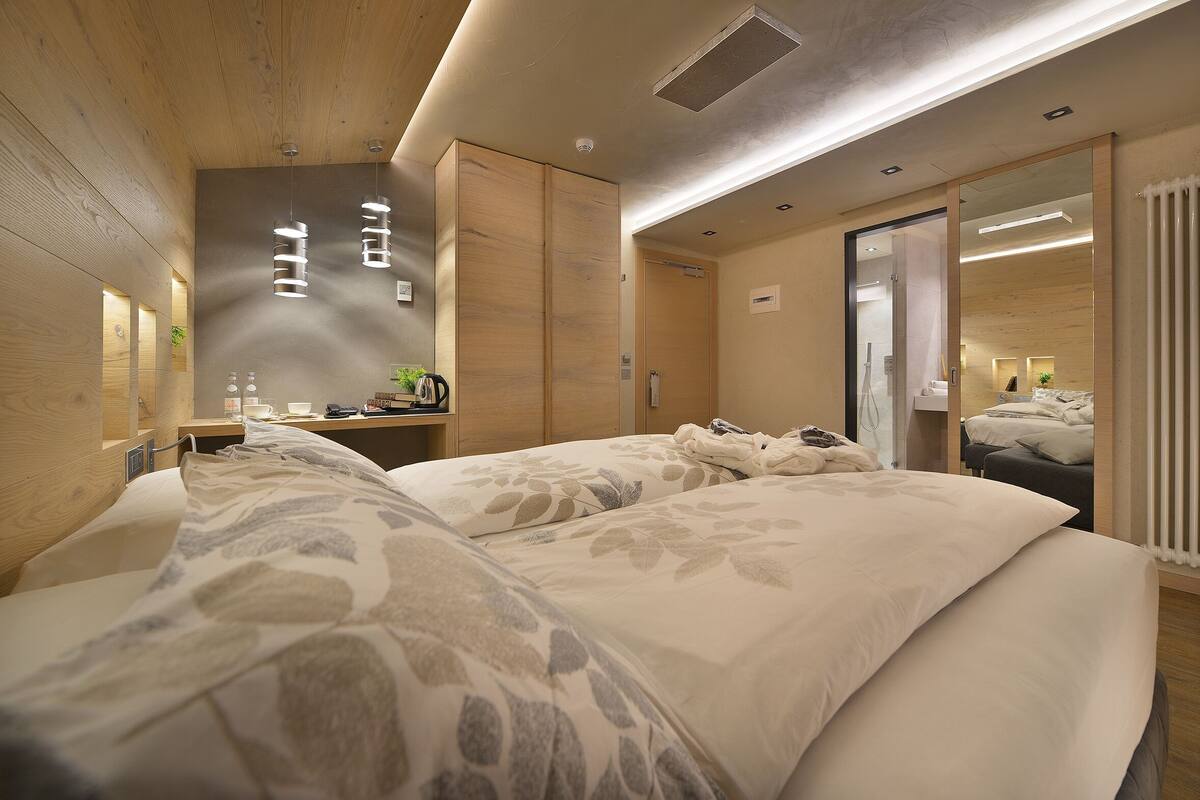 A hotel room with two beds, a wooden ceiling, a large mirror, and a small table with a plant.