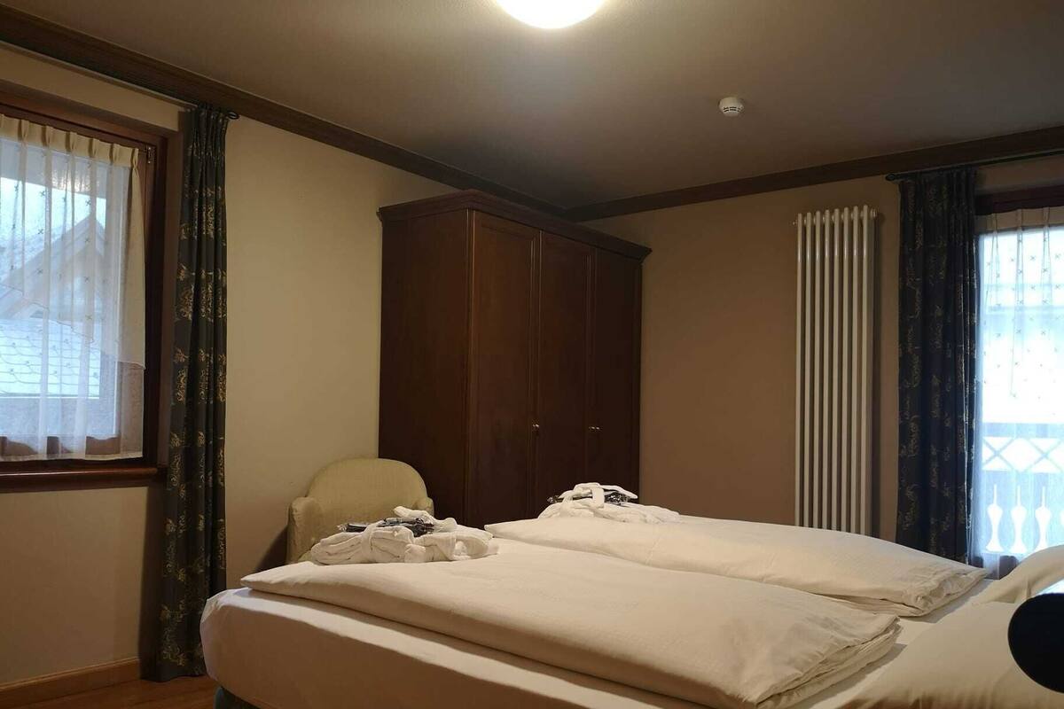 A hotel room with a bed, a wooden wardrobe, a chair, and a radiator.