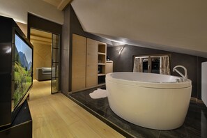 A modern bathroom with a large bathtub, wooden cabinets, and a television displaying a scenic landscape. - Hotel Compagnoni (Livigno)