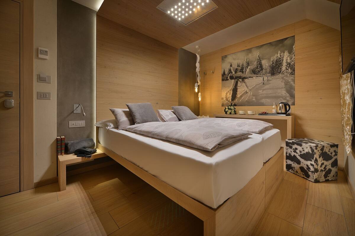 A modern bedroom with a large bed, bedside tables, a nightstand, a painting, and a wooden floor.