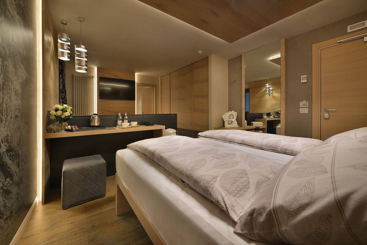 A modern bedroom with a large bed, a bedside table, a mirror, and a small stool.