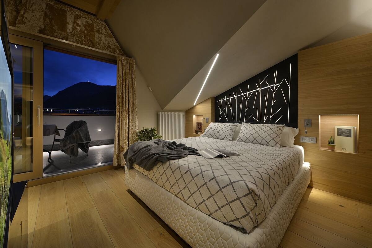 A modern bedroom with a large bed, a view of the mountains, and a cozy seating area by the window.