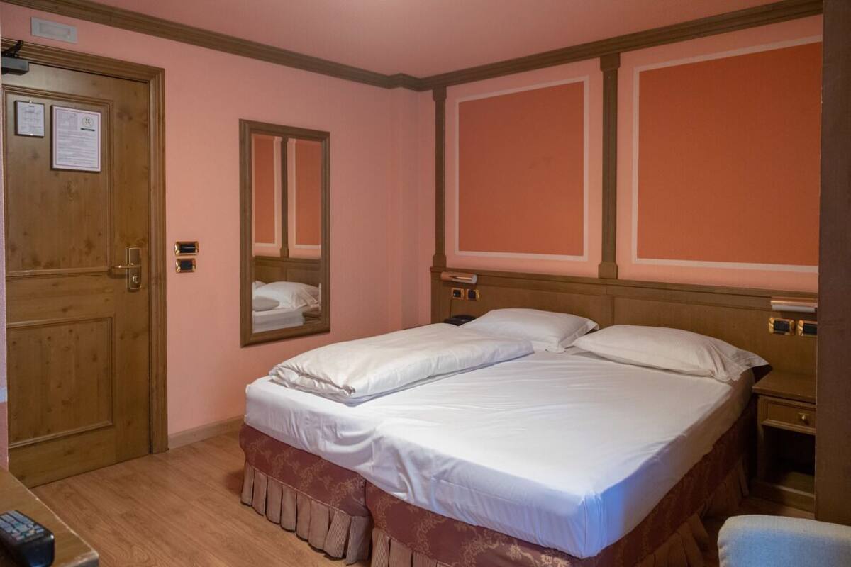 A hotel room with a double bed, a wooden door, a mirror, and a bedside table.