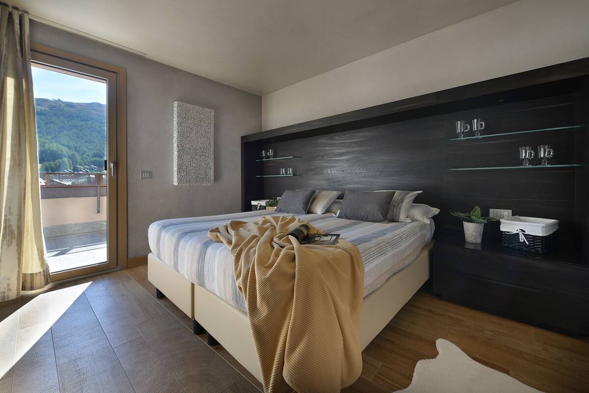 Une chambre moderne avec un grand lit, une tête de lit sombre dotée d ’étagères et une vue sur l’extérieur grâce à une porte coulissante.