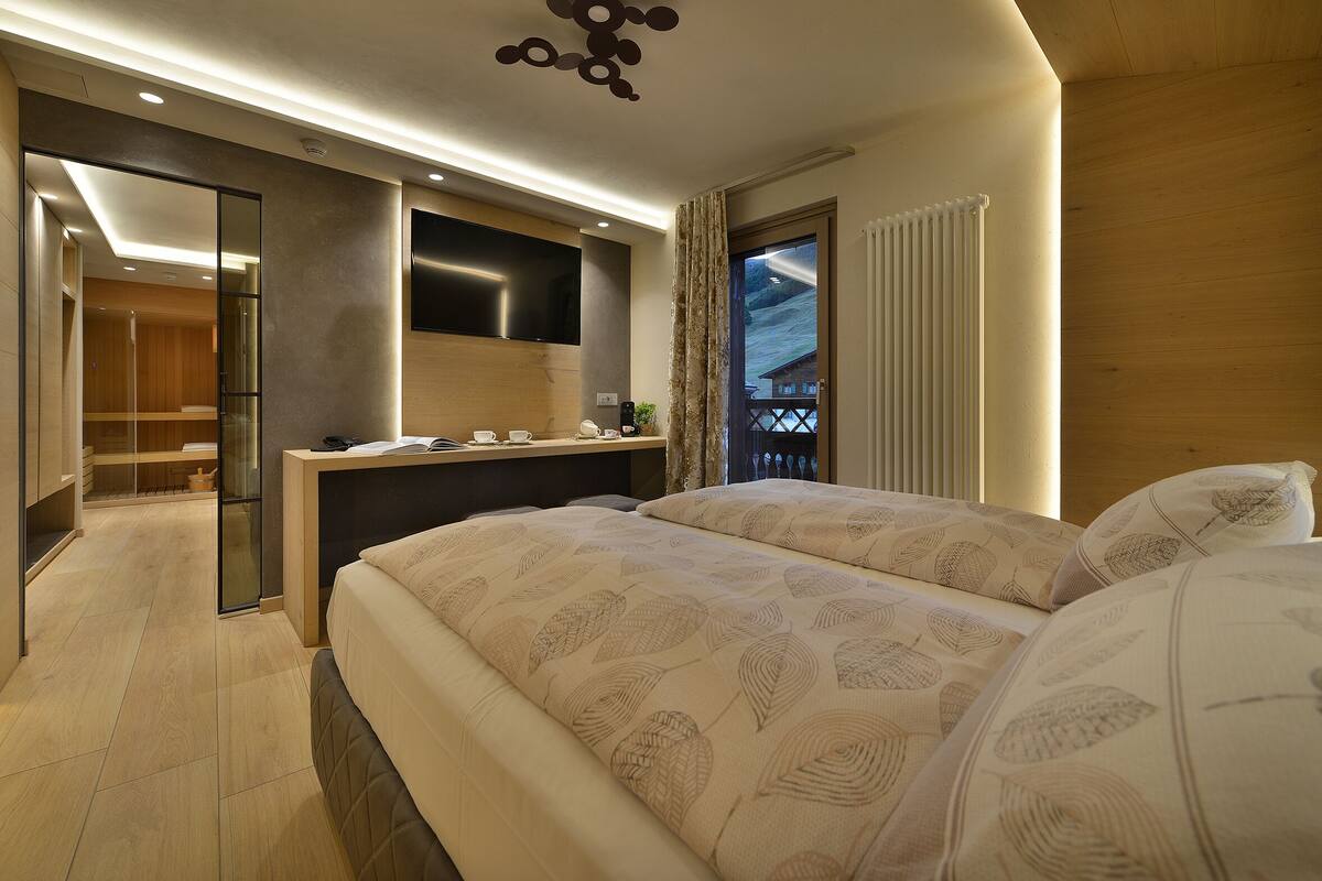 A modern hotel room with a large bed, a desk, and a view of a wooden balcony.