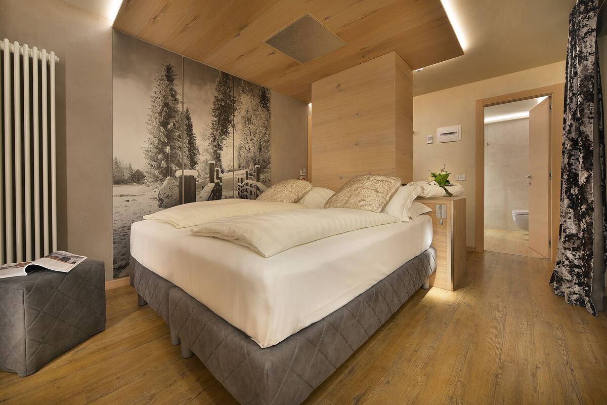 A modern bedroom with a large bed, a bedside table with a lamp, and a wall-mounted radiator.
