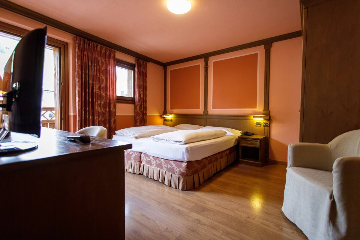 A hotel room with a bed, a desk, a chair, and a nightstand with a lamp.