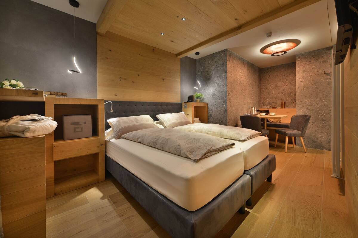 A modern bedroom with a large bed, wooden headboard, bedside tables, and a desk with a chair.