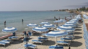 A beach with rows of sun umbrellas and lounge chairs, a calm sea, and a clear sky. - Sporting Club Village (Mazara del Vallo)