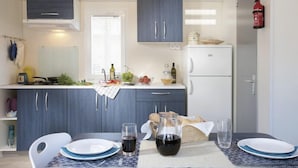 A compact kitchen with dark blue cabinets, a white refrigerator, and a dining table set with plates, glasses, and a pitcher of wine. - Sporting Club Village (Mazara del Vallo)
