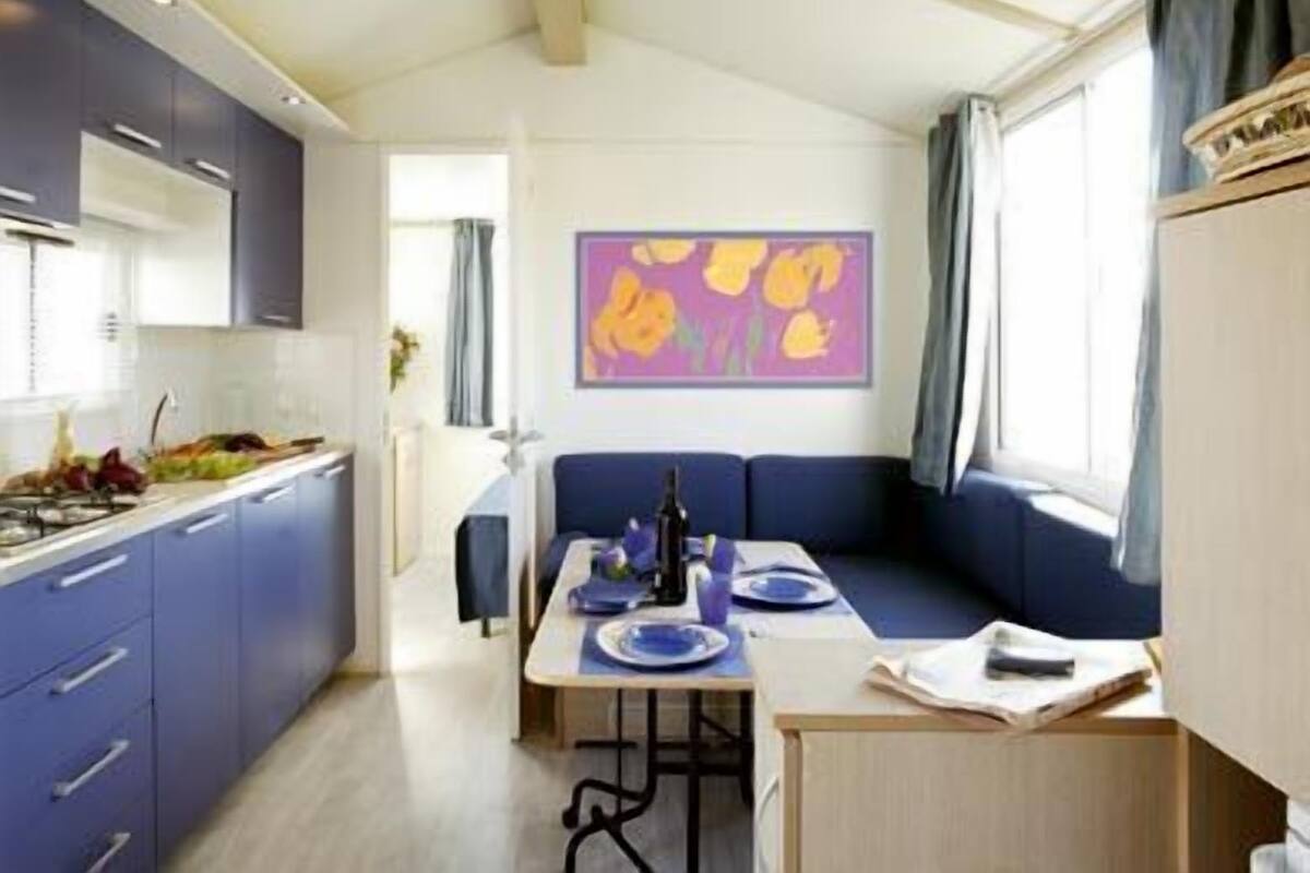 A compact kitchen with modern appliances, a dining area with a table set for two, and a cozy seating area with a window.