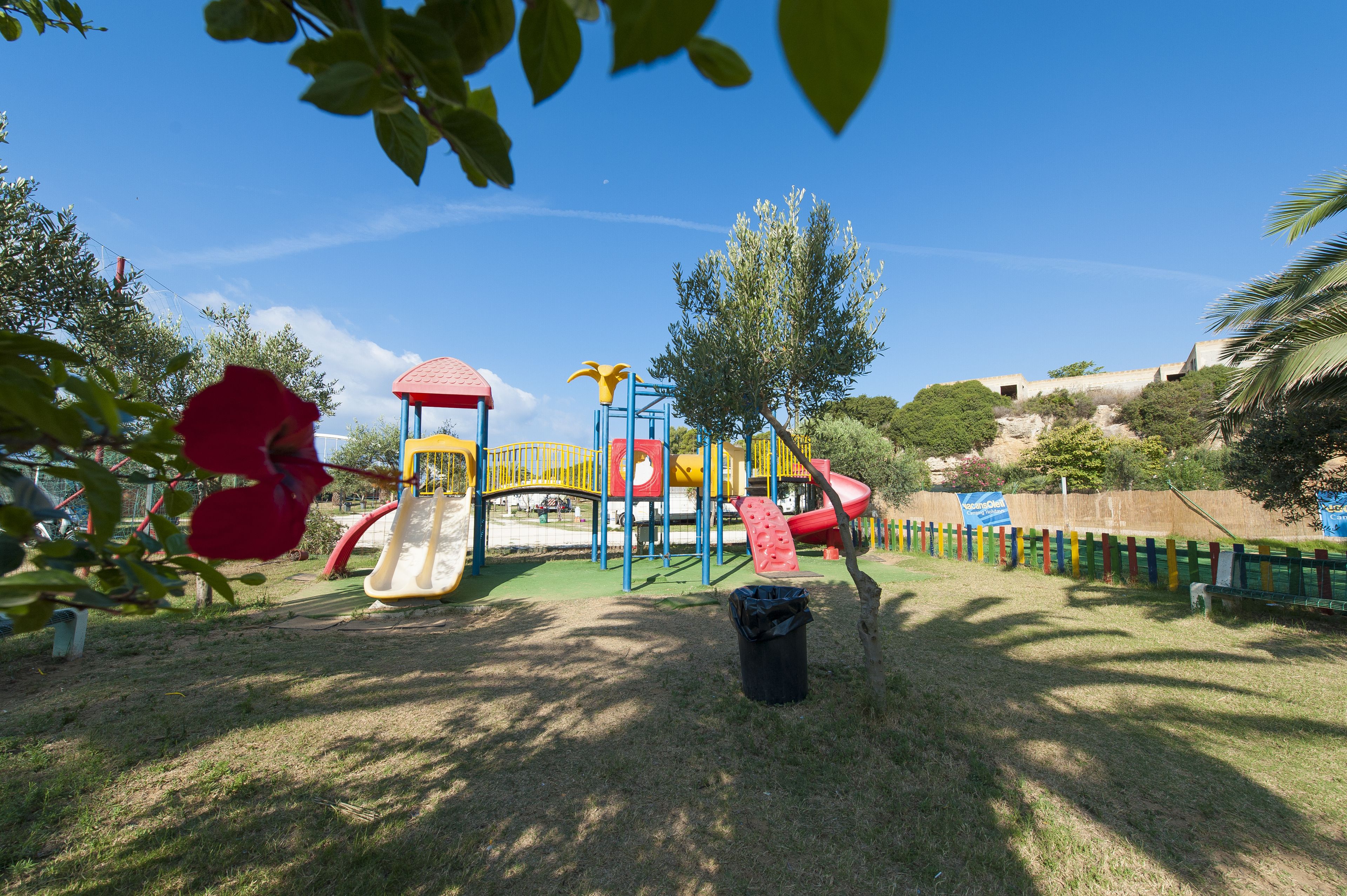 Une aire de jeux avec des toboggans et des structures d’escalade, entourée d’herbe et d’arbres.