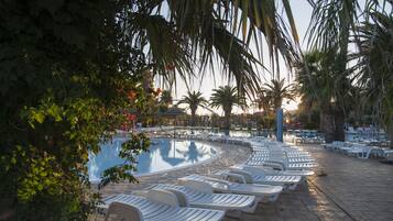 Relax by the serene pool surrounded by lush greenery and palm trees.
