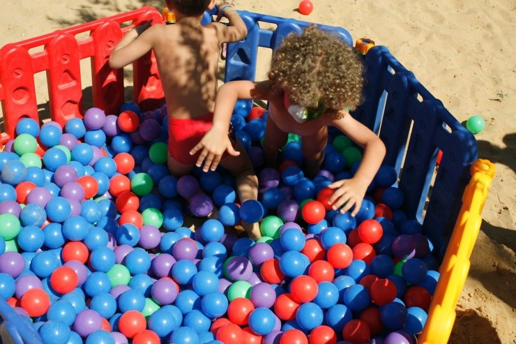 Children playing in a colorful plastic ball pit on a sandy beach.