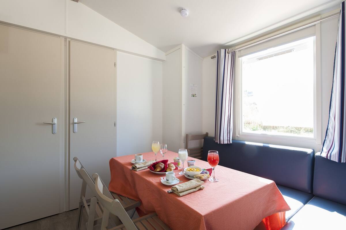 A dining area with a table set for two, a window with curtains, and a view of the outdoors.