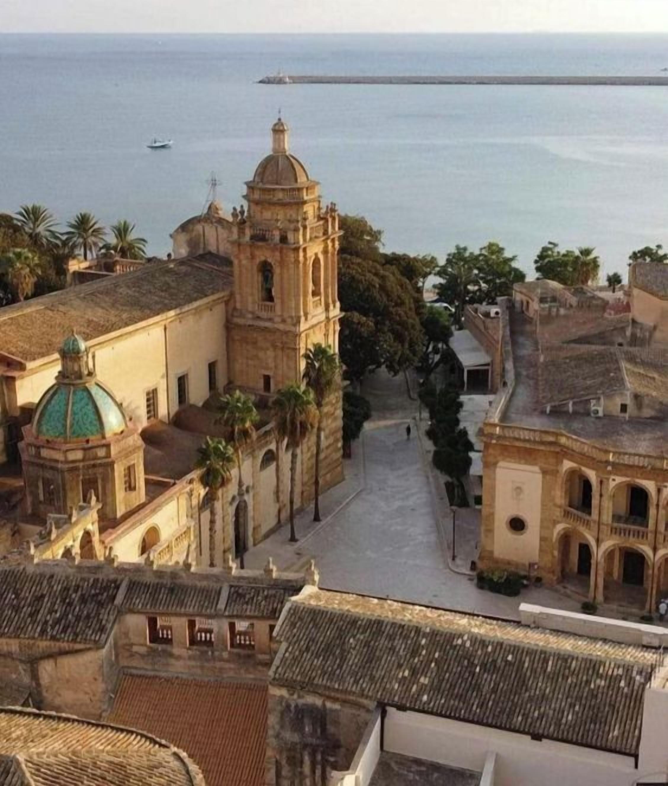 Uma vila costeira com uma igreja imponente, com uma torre de sino e uma cúpula, cercada por palmeiras e edifícios com arquitetura tradicional.