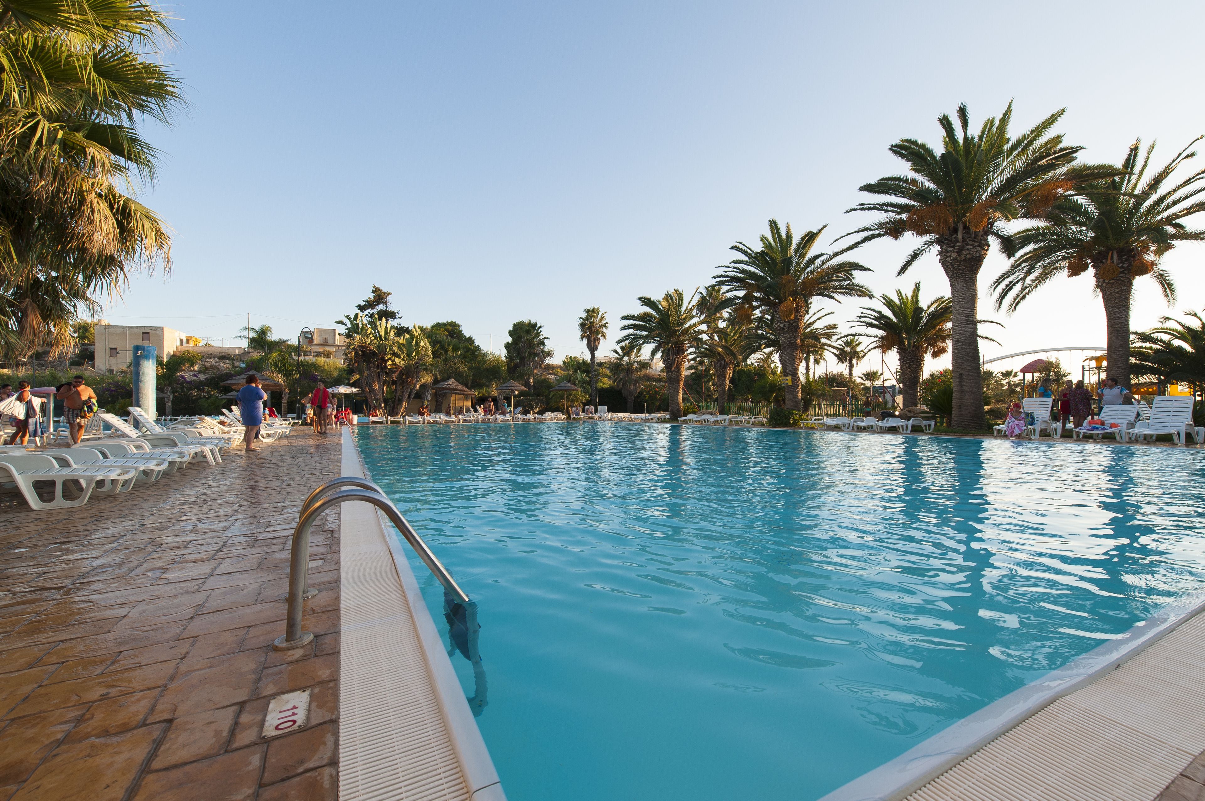 Una piscina con sillones de descanso y palmeras.