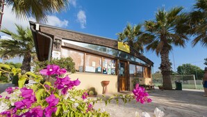 A reception area with a wooden facade, palm trees, and vibrant flowers. - Sporting Club Village (Mazara del Vallo)