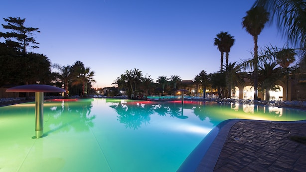 A swimming pool with lounge chairs and palm trees. - Sporting Club Village (Mazara del Vallo)