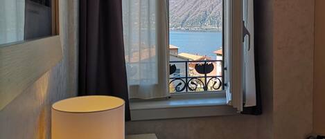 A room with a table, a lamp, a window with a view of a lake and mountains, and a chair.