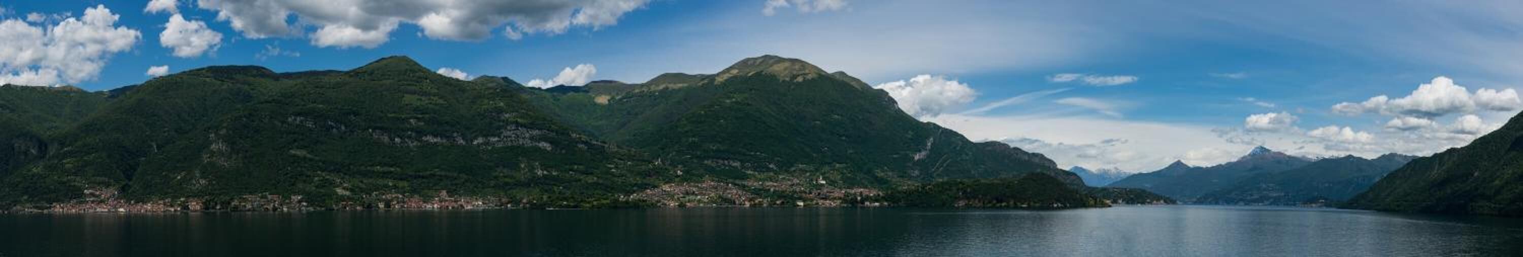 A panoramic view of a mountainous landscape with a body of water in the foreground and a town on the opposite shore.