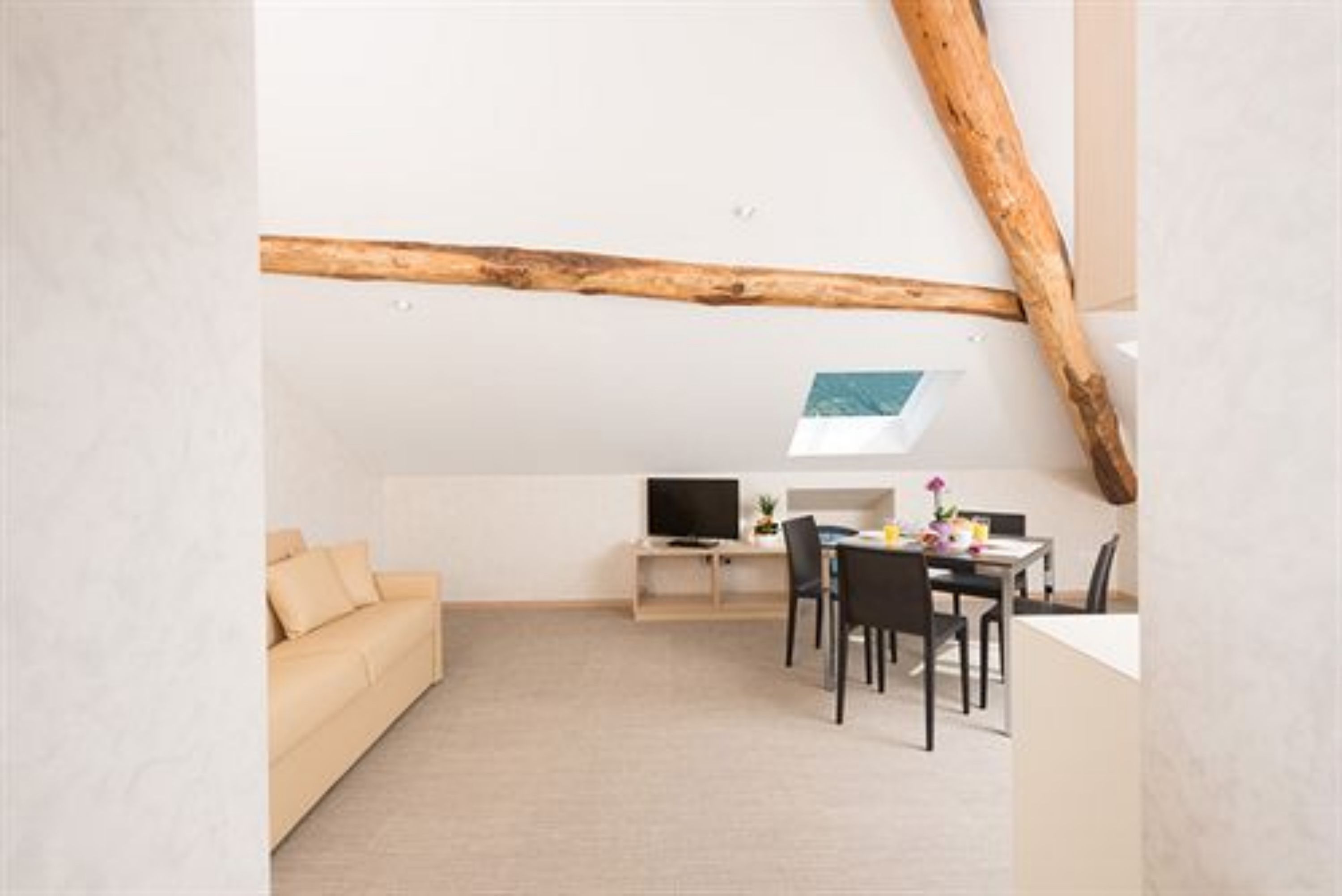 Un espacio habitable moderno y minimalista, con techo alto, vigas de madera a la vista, un sofá, una mesa de comedor con sillas y un televisor de pantalla plana.