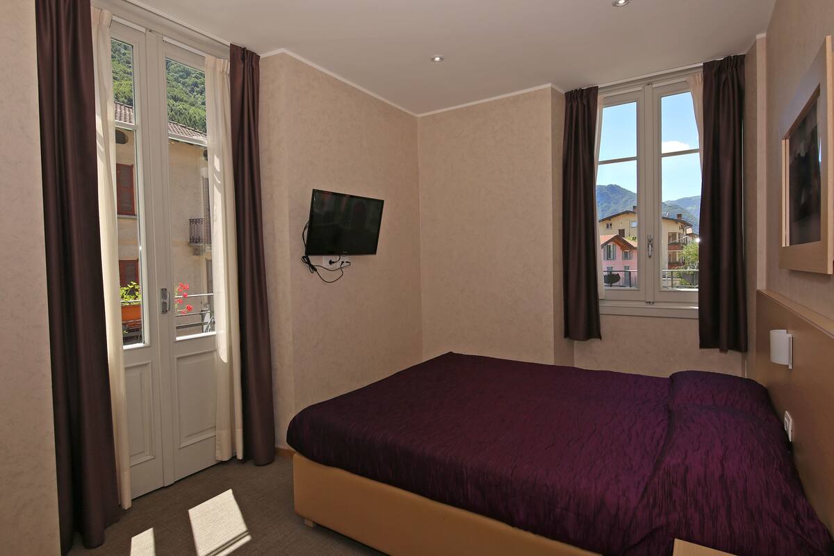 Un dormitorio con cama, televisor montado en la pared y ventana con cortinas.