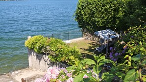 Een tuin aan het meer met een stenen muur, een metalen hek en een bank.