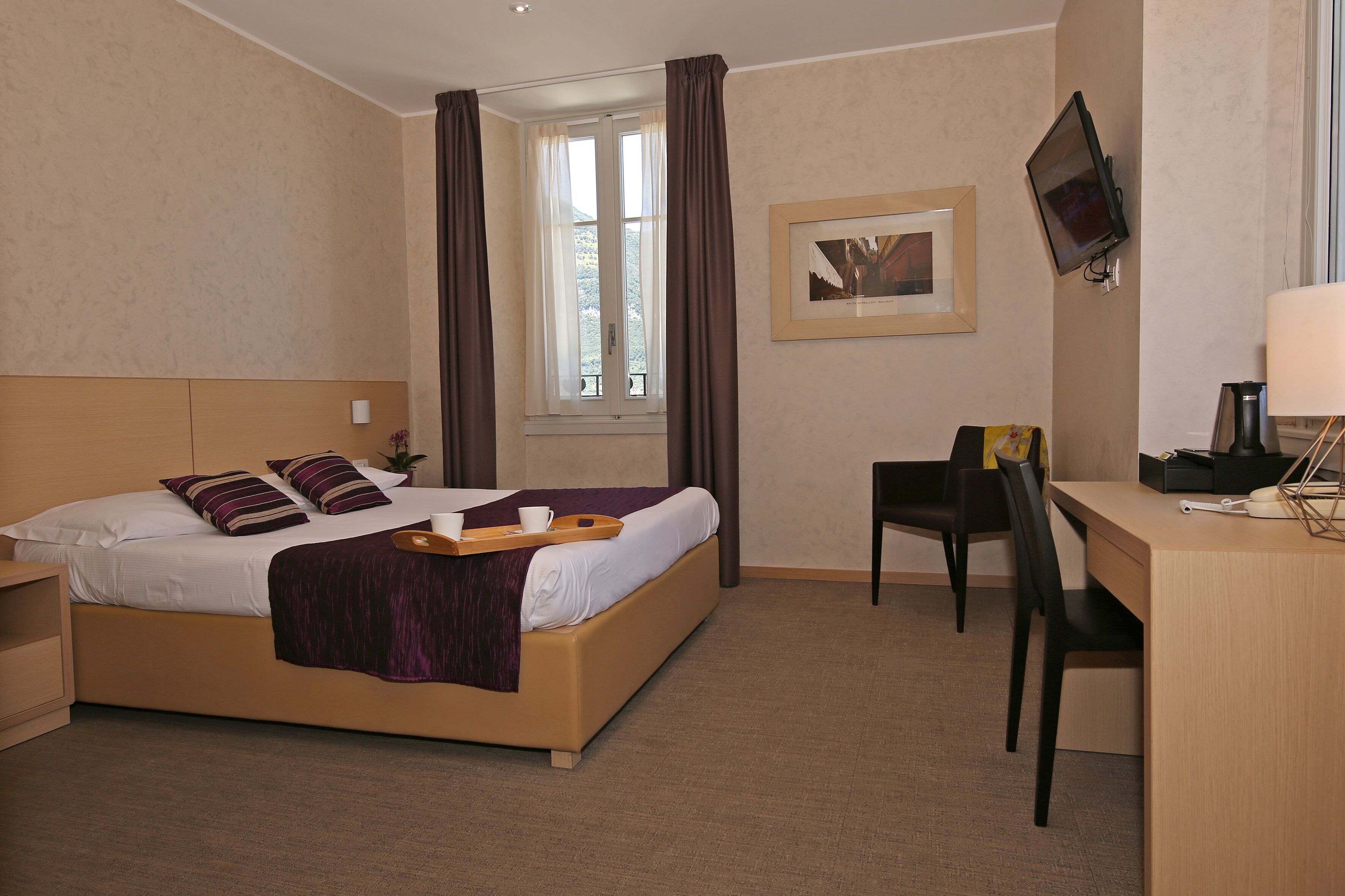 A hotel room with a bed, a desk, a chair, a TV, and a window with curtains.