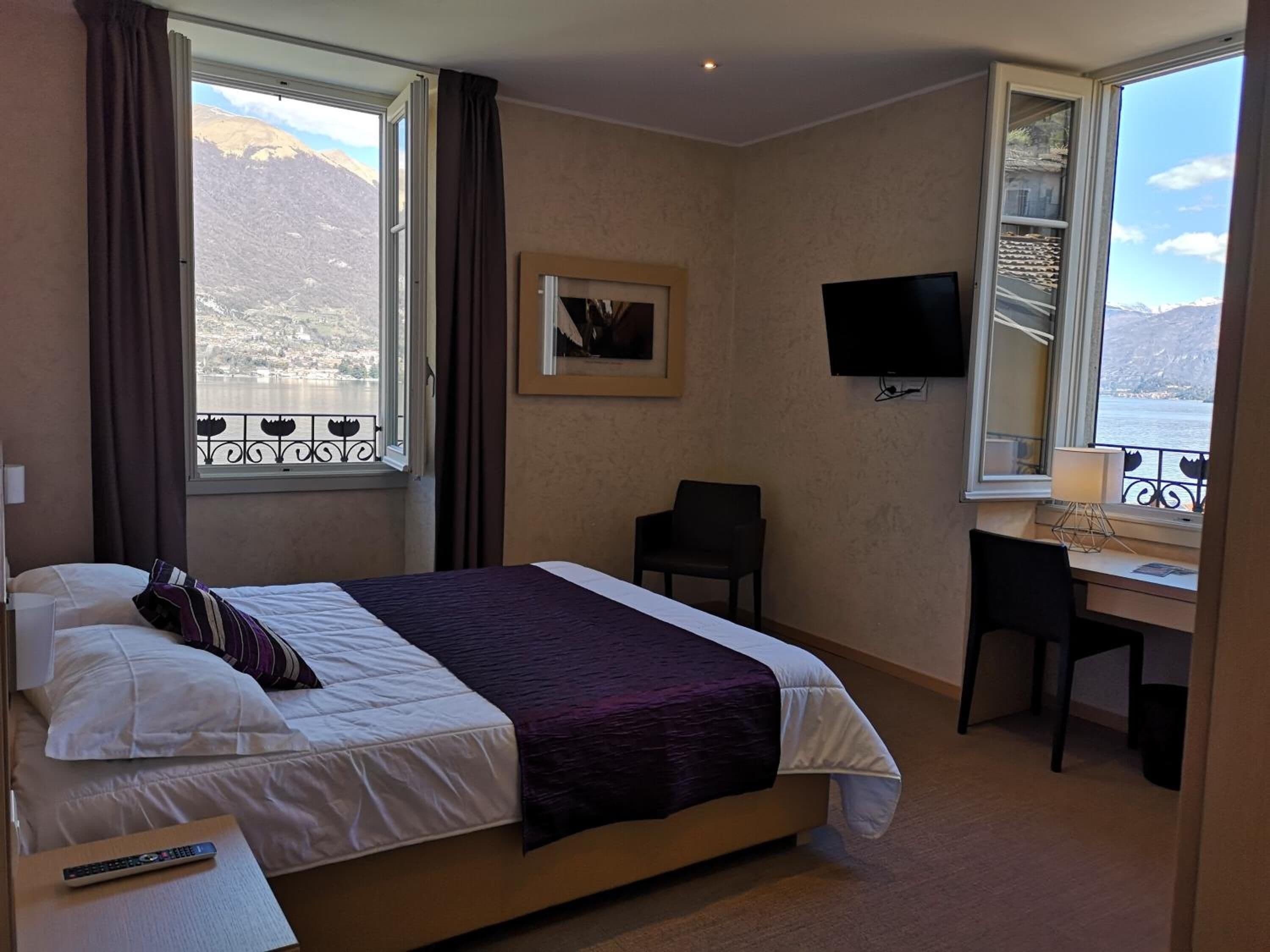 Une chambre d’hôtel équipée d’un lit, d’un bureau, d’une chaise, d’une télévision et d’une fenêtre donnant sur les montagnes.
